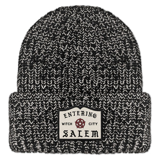 Black and white marled knit beanie with 'Entering Witch City Salem' embroidered patch on a white background