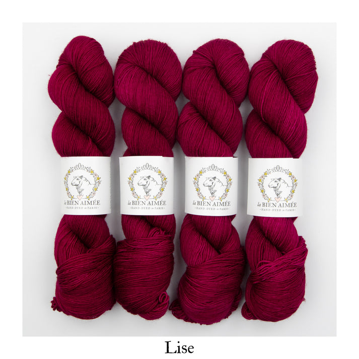 An image of four skeins of sock yarn in a vibrant fuscia color with white ‘La Bien Aimee’ labels against a white background.
