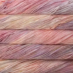 A close up of skeins of Malabrigo Rios worsted weight yarn in light beige, purple, and pink colors