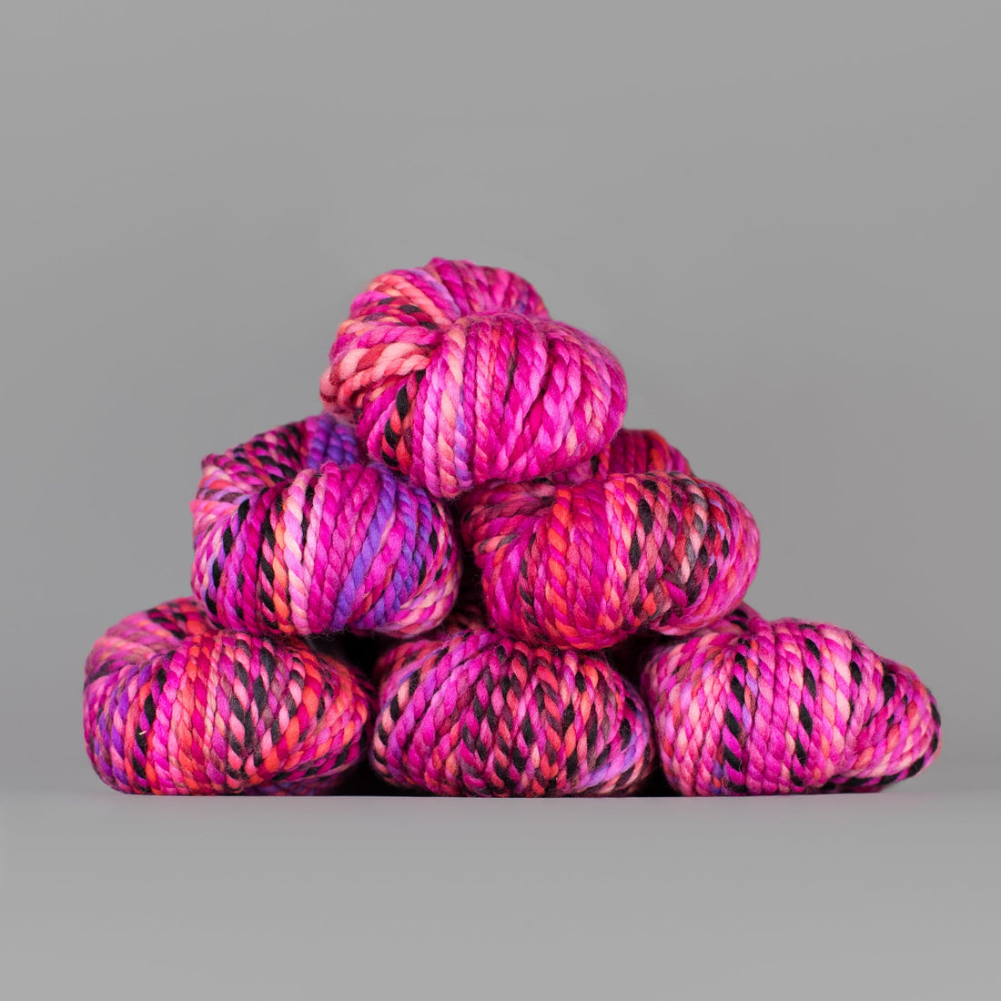 Skeins of Spincycle Plump Bulky weight yarn in pink, black, and purple color gradient