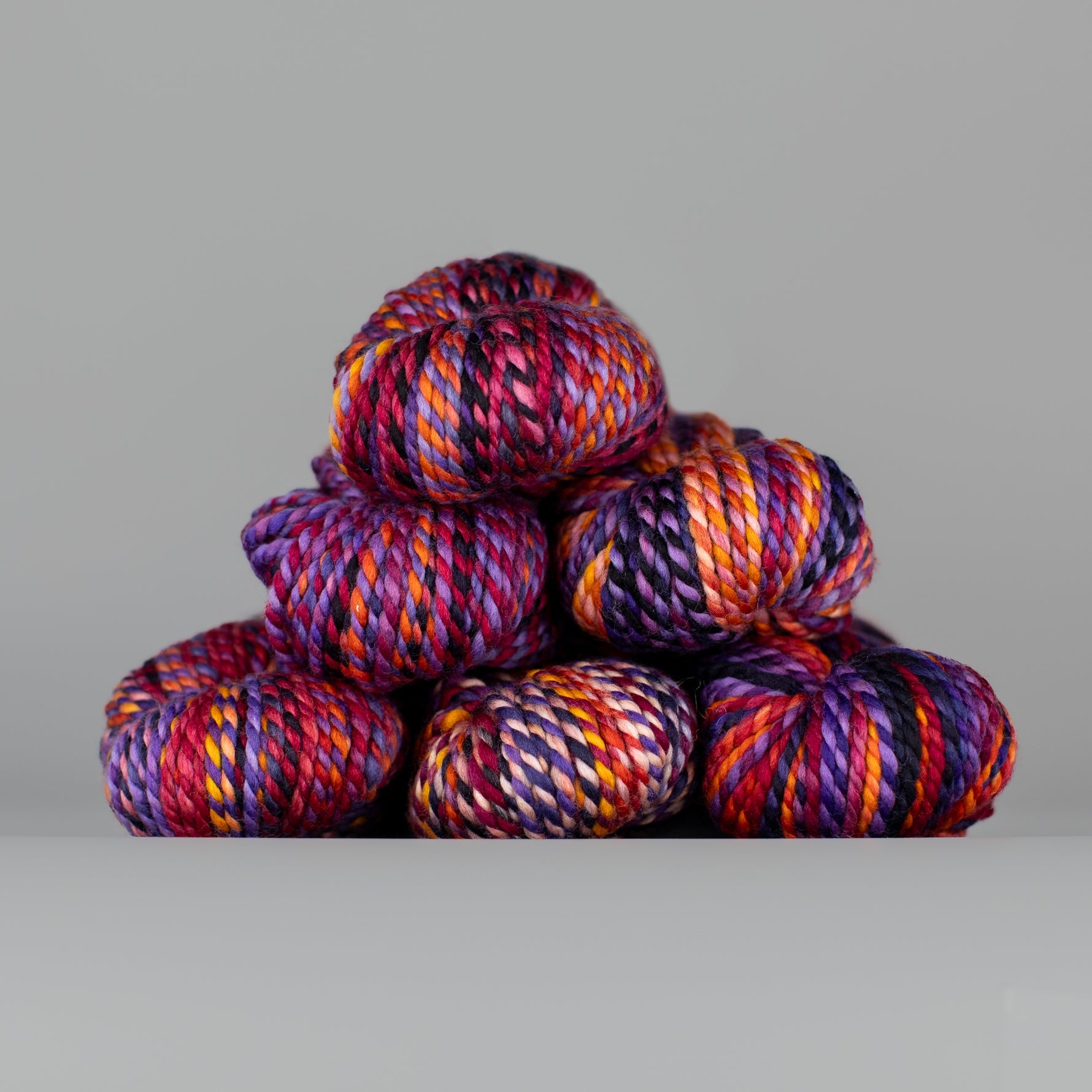 Skeins of Spincycle Plump Bulky weight yarn in pink, purple, orange, red, and black color gradient