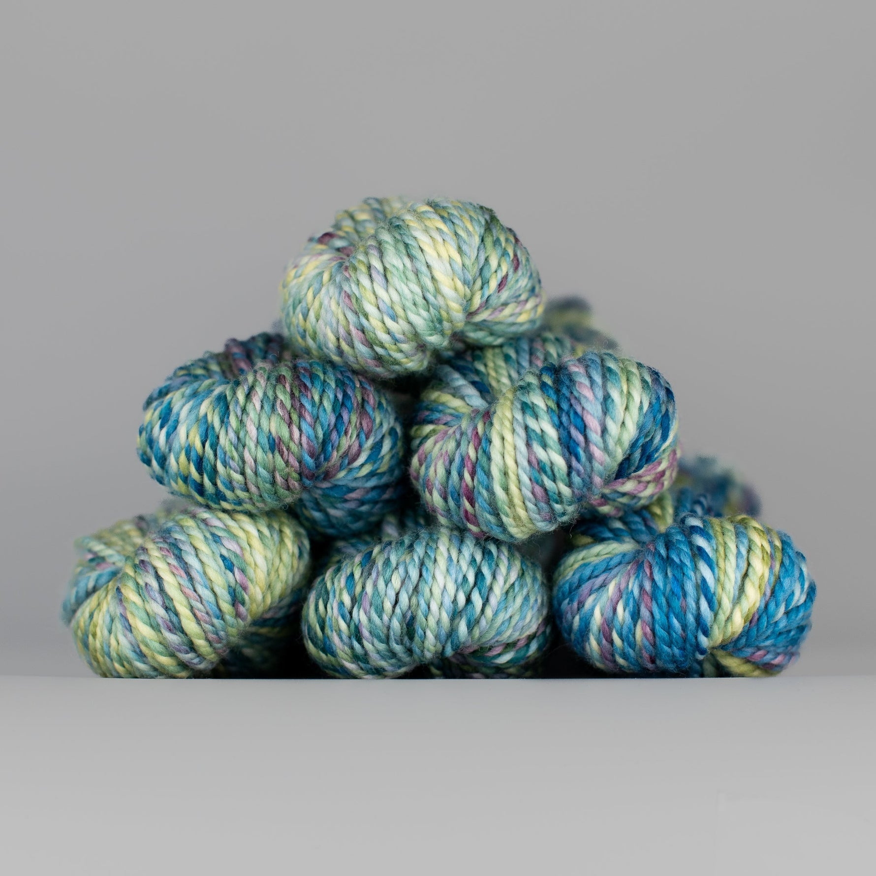 Skeins of Spincycle Plump Bulky weight yarn in pale green, aqua blue, yellow, and purple color gradient