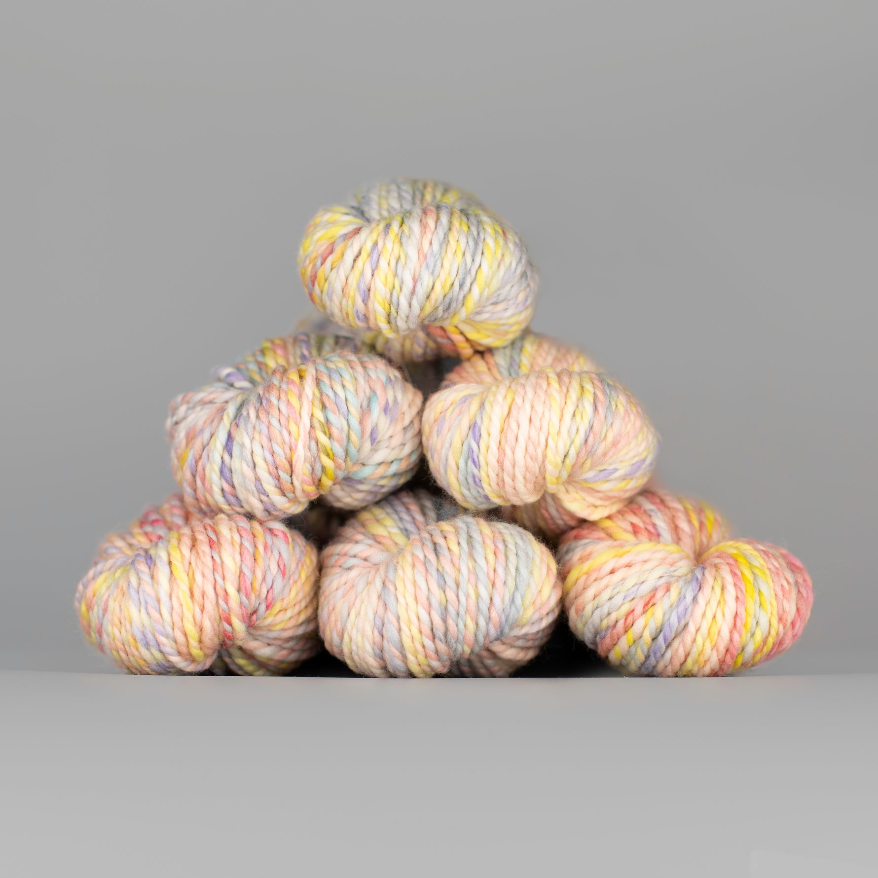 Skeins of Spincycle Plump Bulky weight yarn in pale pink, yellow, blue, and purple color gradient