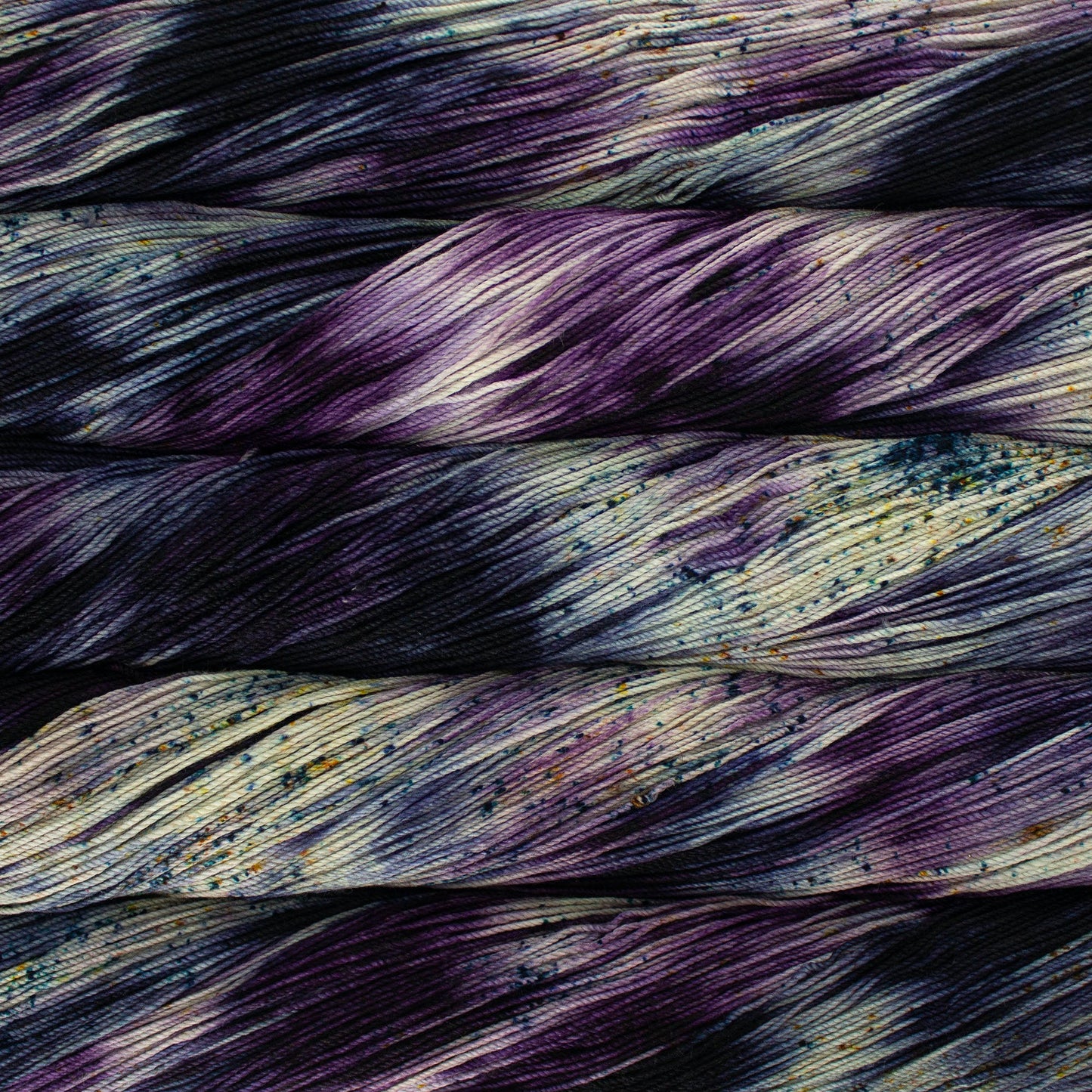 A close-up image of skeins of Malabrigo Sock yarn in cream and dark purple, with speckles of blue and yellow.