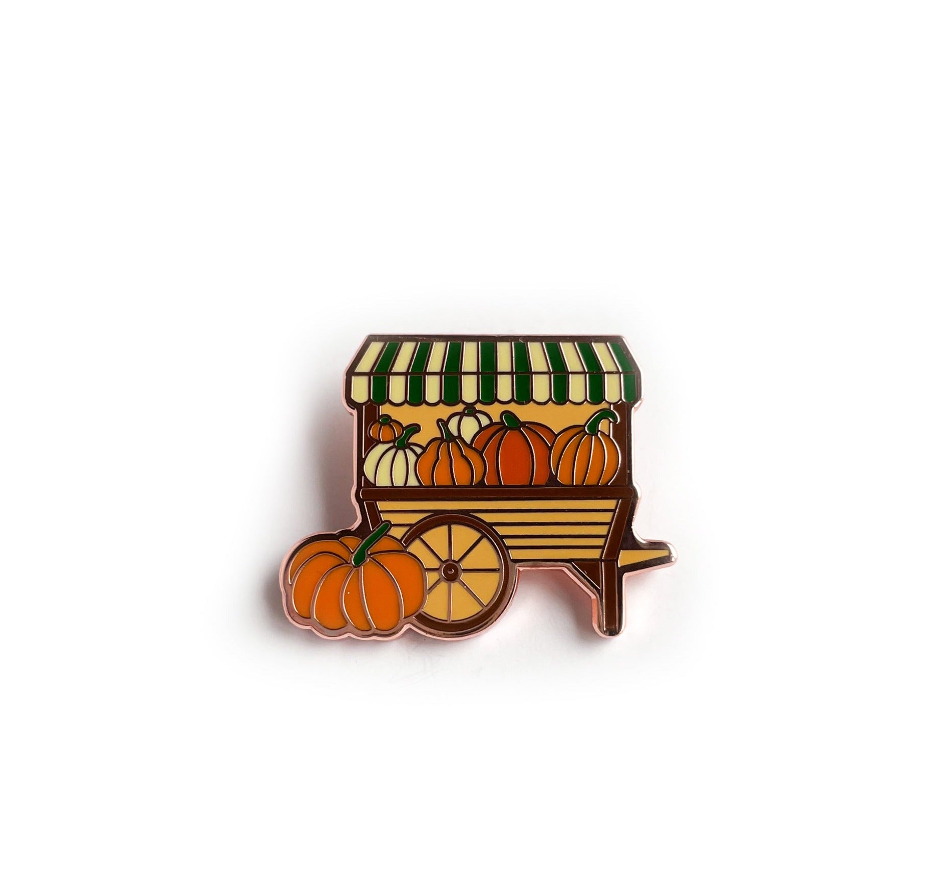 An enamel pin shaped like a pumpkin cart with a green striped roof and full of different colored pumpkins.