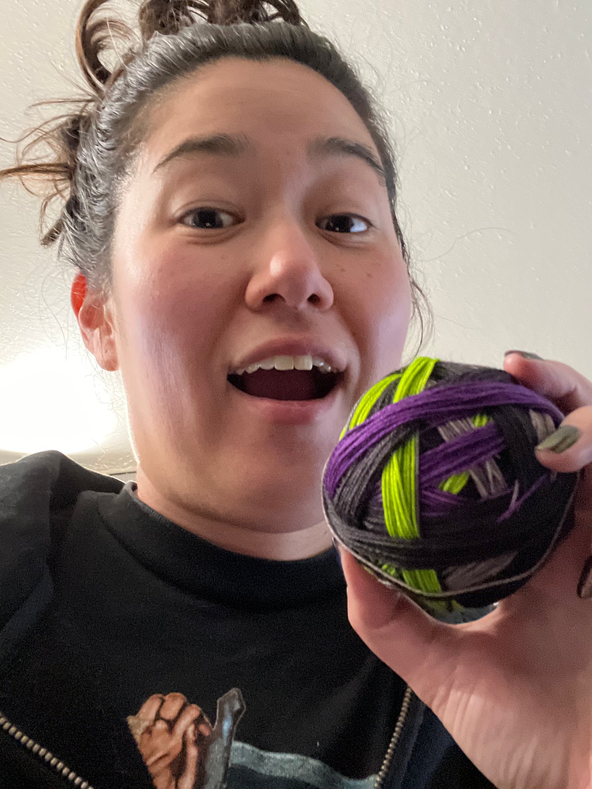 BIPOC woman holding a ball of purple, acid green, black, and gray hand dyed yarn