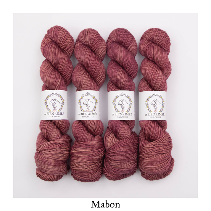 An image of four skeins of DK weight yarn in shades of dusty red with white ‘La Bien Aimee’ labels against a white background.