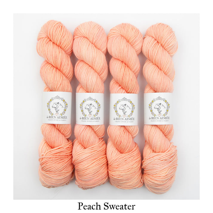 An image of four skeins of DK weight yarn in a peach pink color with white ‘La Bien Aimee’ labels against a white background.