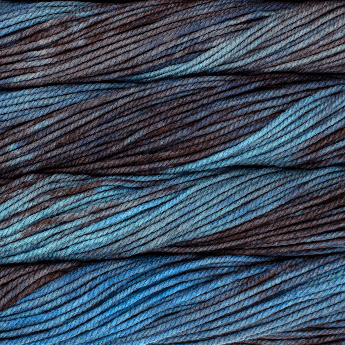 A close up image of skeins of Malabrigo Chunky bulky weight yarn in bright blue and charcoal shades.