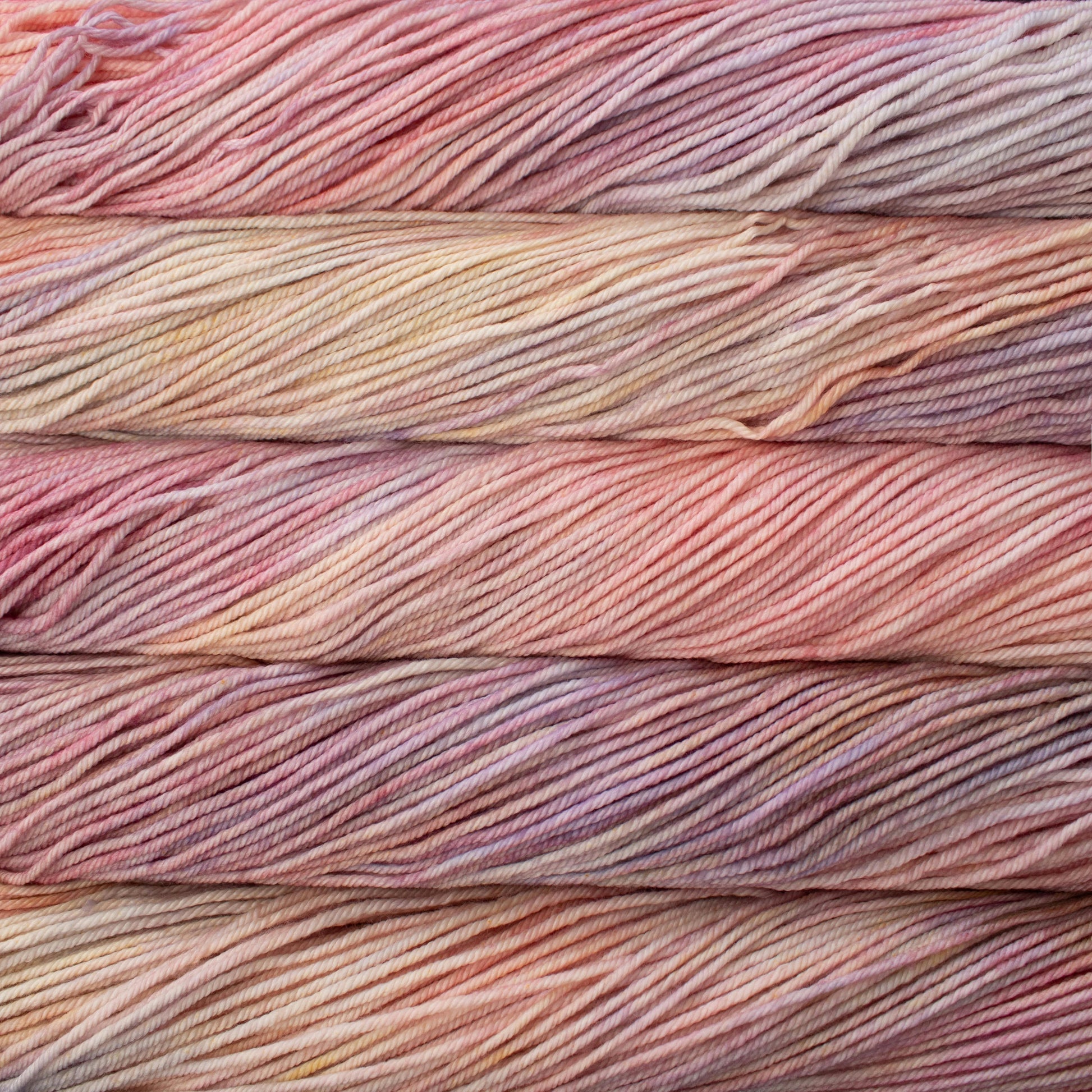A close up of skeins of Malabrigo Rios worsted weight yarn in light beige, purple, and pink colors.