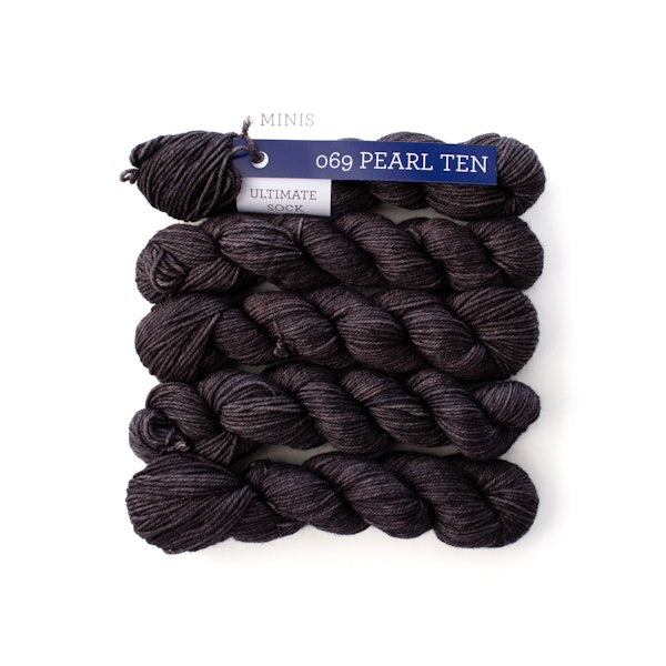 Multiple mini skeins of Malabrigo Ultimate Sock Pearl Ten, dark gray with purple undertones sock yarn against a white background