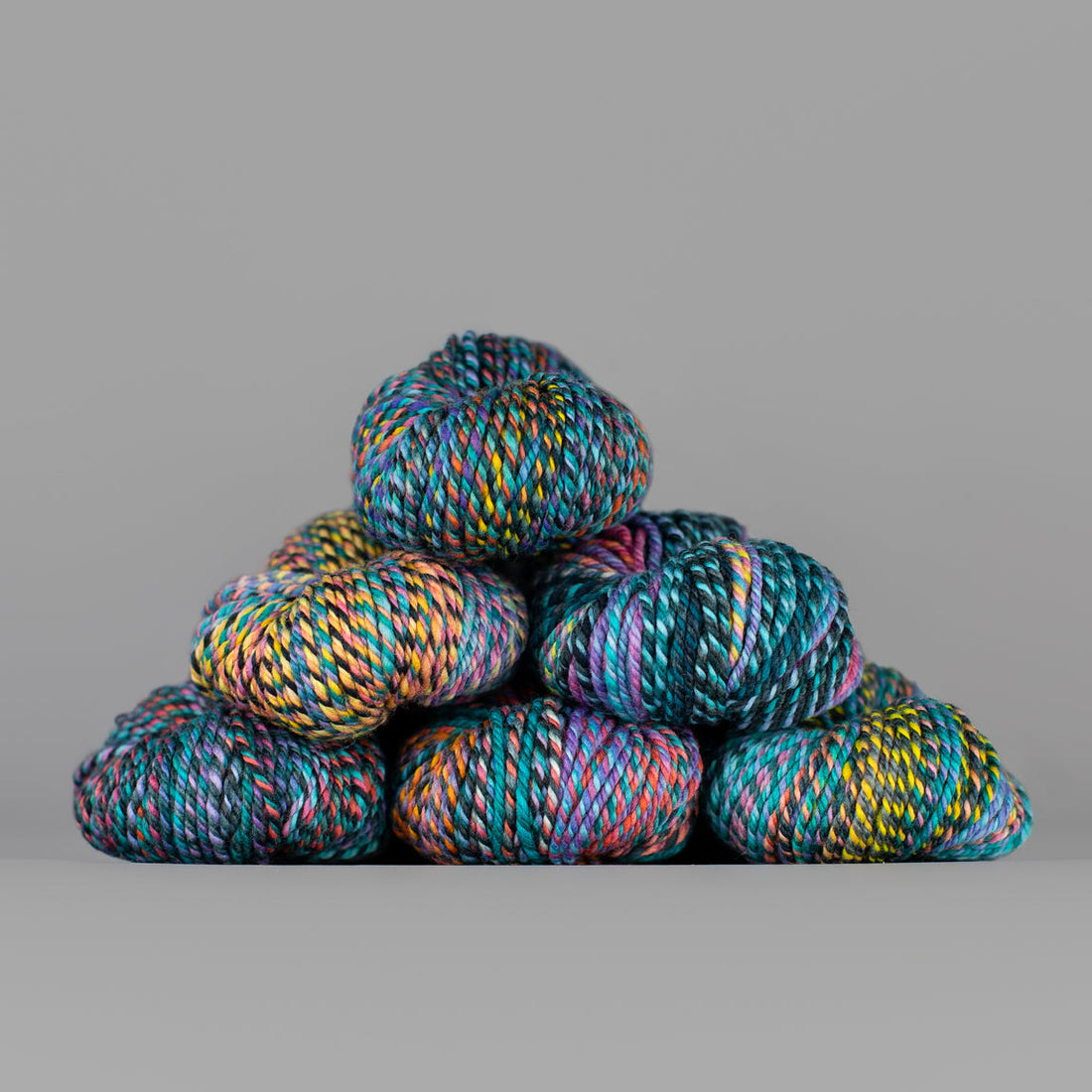 An image of skeins of Spincycle Dream State worsted weight yarn in a blue, yellow, pink, and purple color gradient against a gray background.