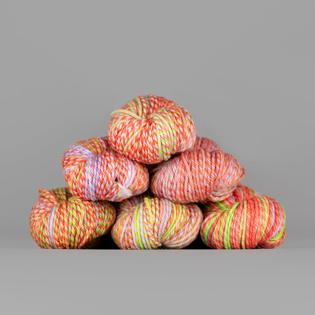 An image of skeins of Spincycle Dream State worsted weight yarn in a neon yellow green, and orange pink color gradient against a gray background.