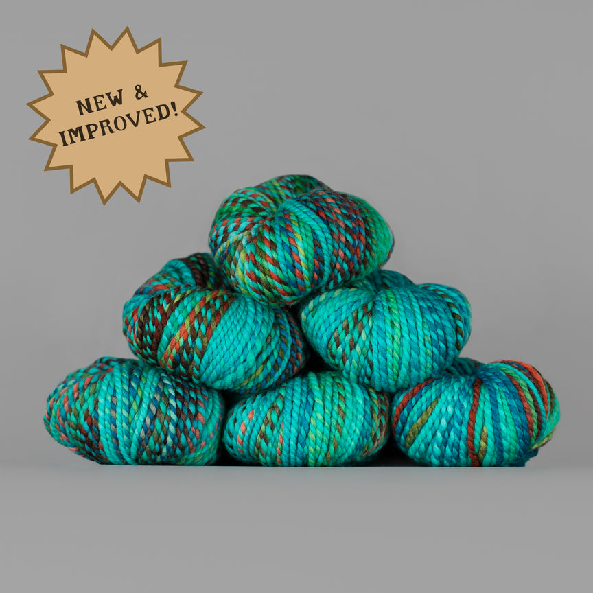A stack of variegated yarn skeins in bright teal, turquoise, and green with thin red and orange stripes, set against a solid gray background with a tan starburst badge that reads 'NEW & IMPROVED!'.