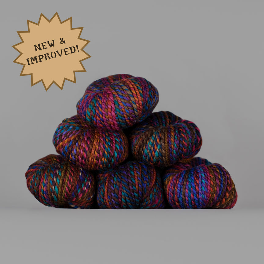 A stack of seven variegated yarn skeins in a dark base with bright purple, blue, pink, and orange highlights, set against a solid gray background with a tan starburst badge that reads 'NEW & IMPROVED!'.