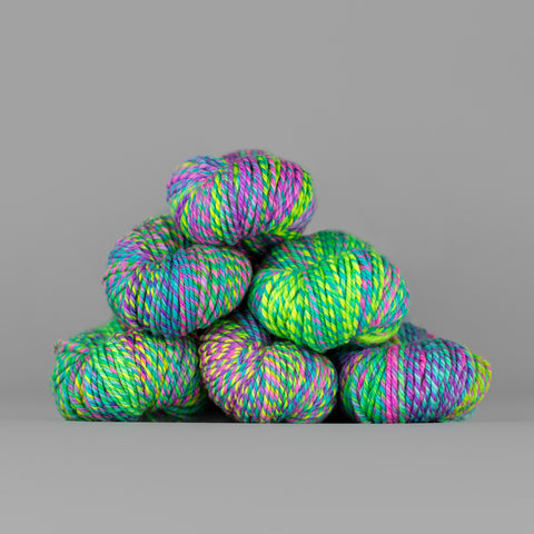 An image of skeins of Spincycle Dream State worsted weight yarn in a neon green, blue, pink, and purple color gradient against a gray background.
