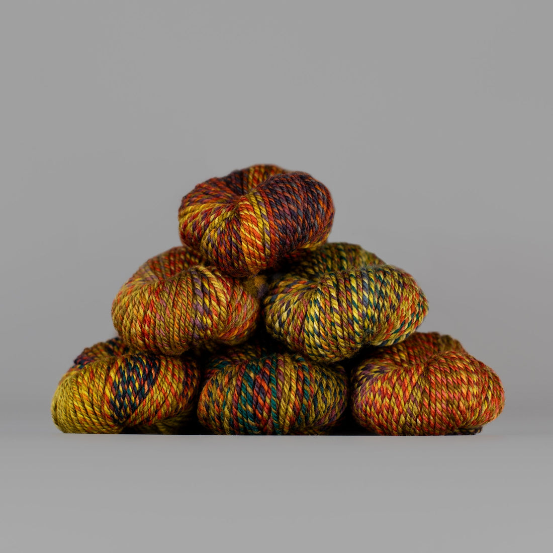 An image of skeins of Spincycle Dream State worsted weight yarn in an orange, red, teal, and yellow color gradient against a gray background.