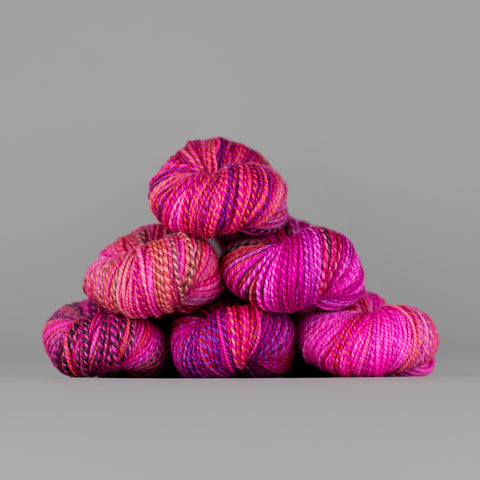 Skeins of Spincycle Dyed in the Wool sport weight yarn in a hot pink, purple, and red color gradient against a gray background.