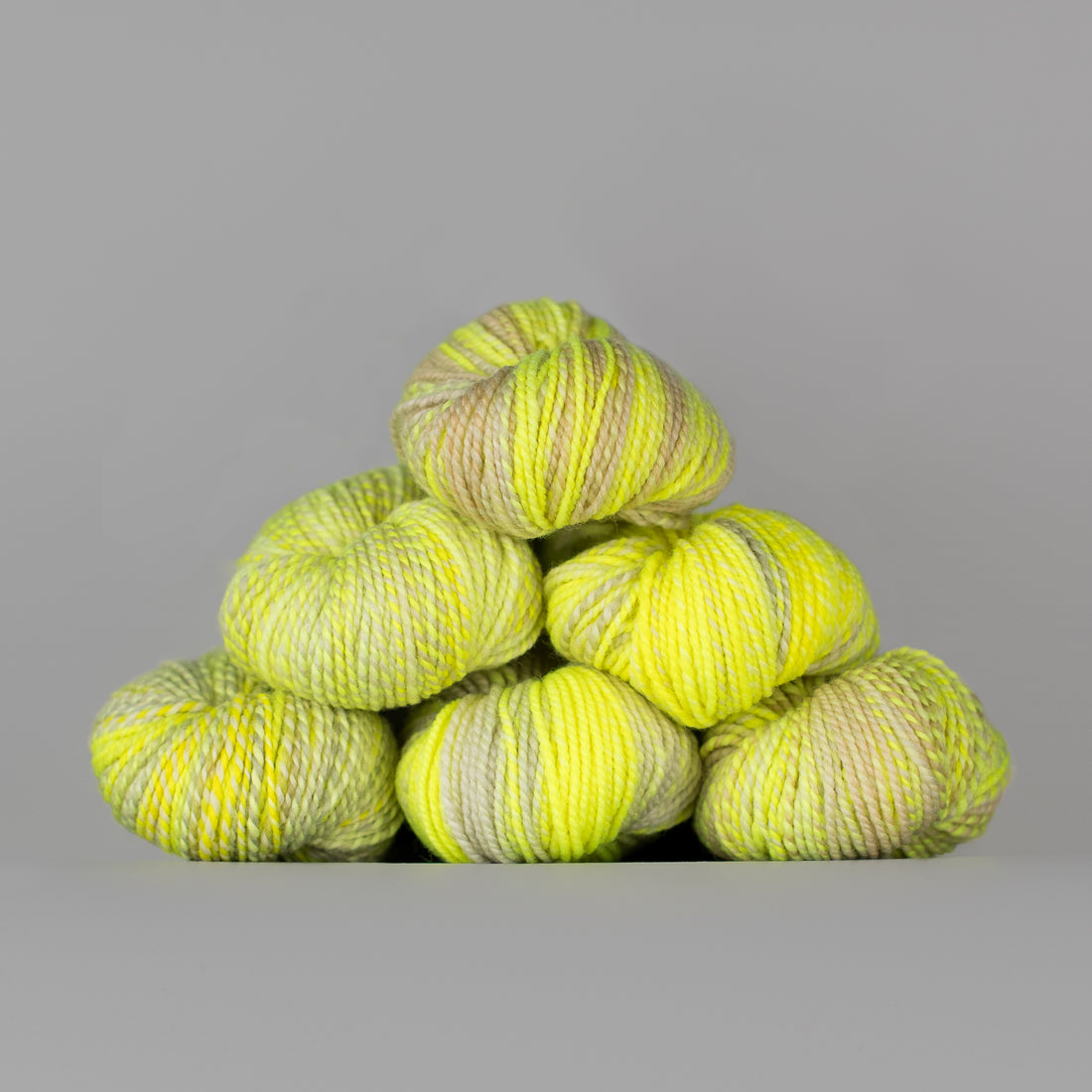 Skeins of Spincycle Dyed in the Wool sport weight yarn in a neon yellow and tan color gradient against a gray background.