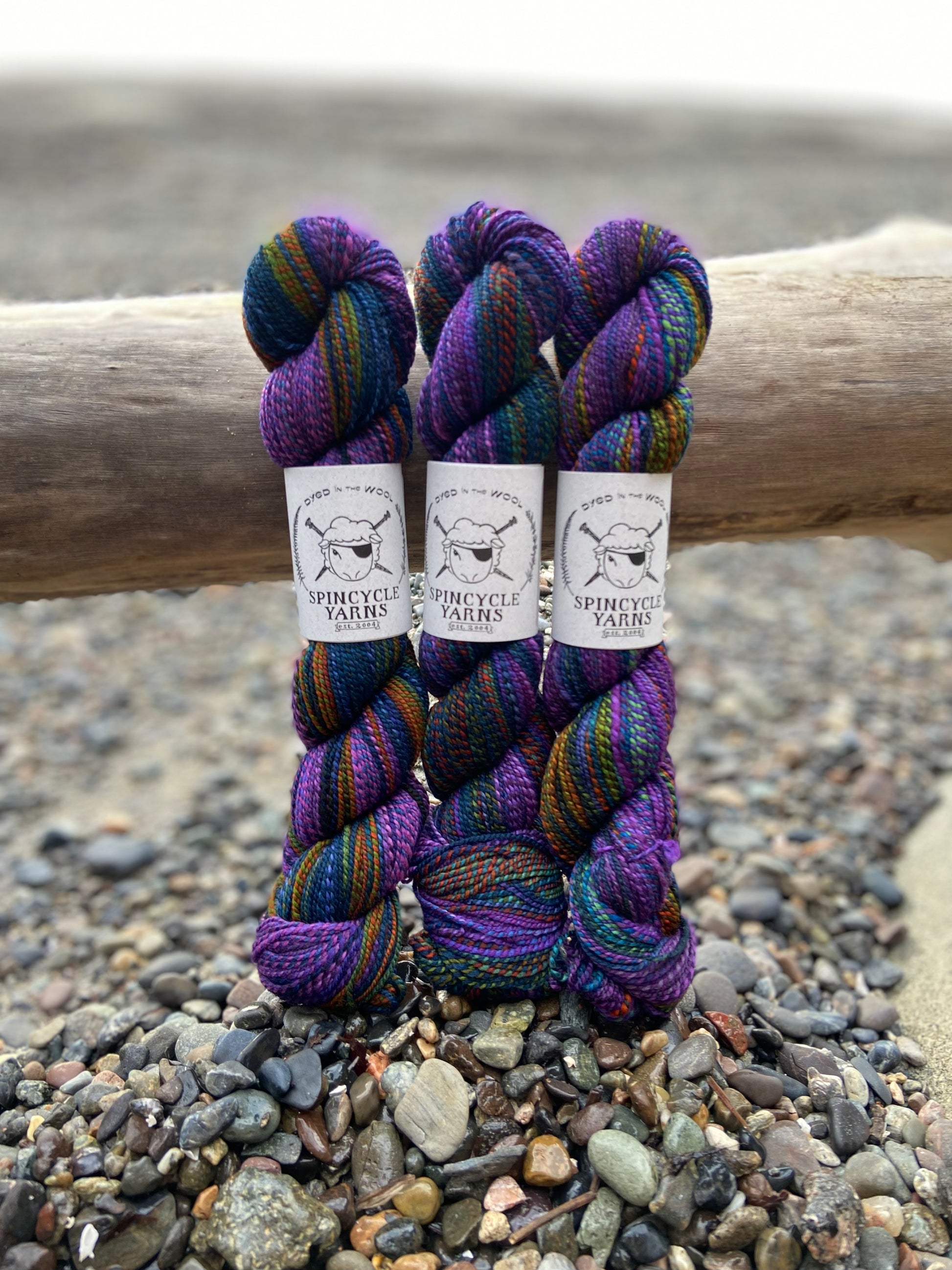 Multiple skeins of Spincycle sport weight yarn in a blue, green, orange, and purple color gradient, with labels showing the brand 'Spincycle Yarns'.