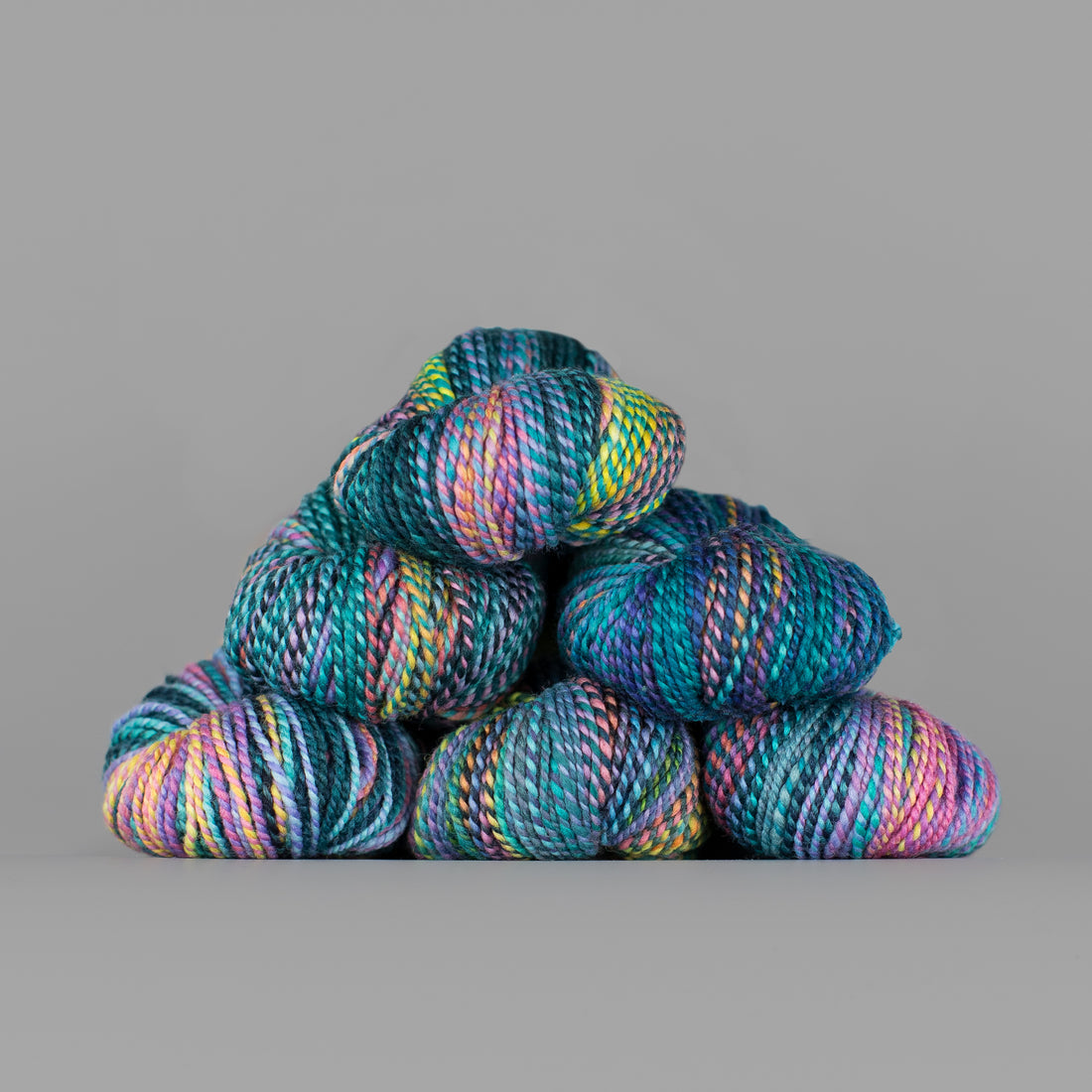 Skeins of Spincycle Dyed in the Wool sport weight yarn in a teal, green, yellow, and pink color gradient against a gray background.