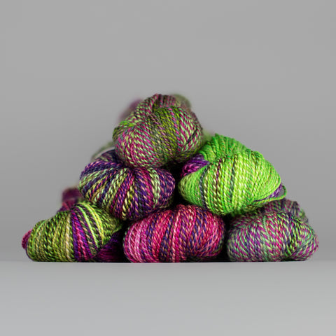 Skeins of Spincycle Dyed in the Wool sport weight yarn in a neon green, hot pink, and purple color gradient against a gray background.