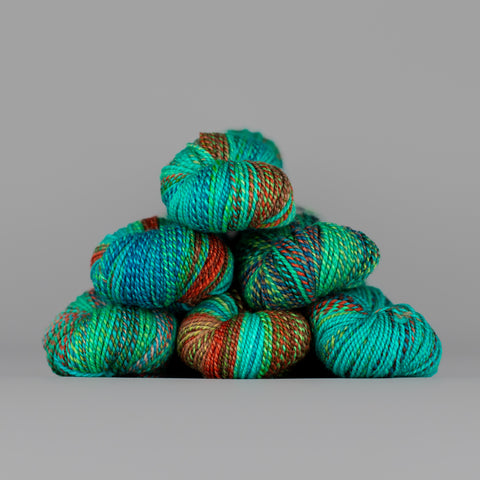 Skeins of Spincycle Dyed in the Wool sport weight yarn in an aqua green, blue, and red color gradient against a gray background.