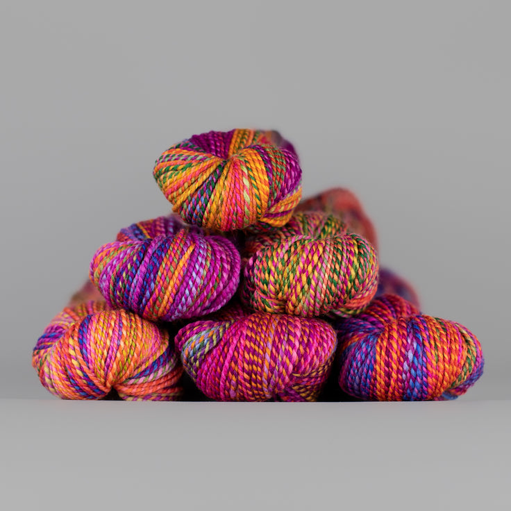 Skeins of Spincycle Dyed in the Wool sport weight yarn in a vibrant rainbow of colors against a gray background.