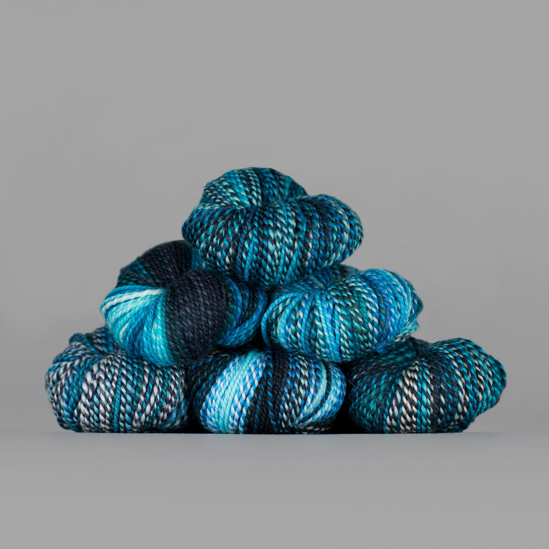 Skeins of Spincycle Dyed in the Wool sport weight yarn in a sky blue, navy, teal, and gray color gradient against a gray background.