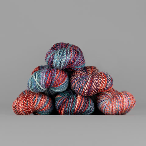Skeins of Spincycle Dyed in the Wool sport weight yarn in a red orange, gray blue, and purple color gradient against a gray background.