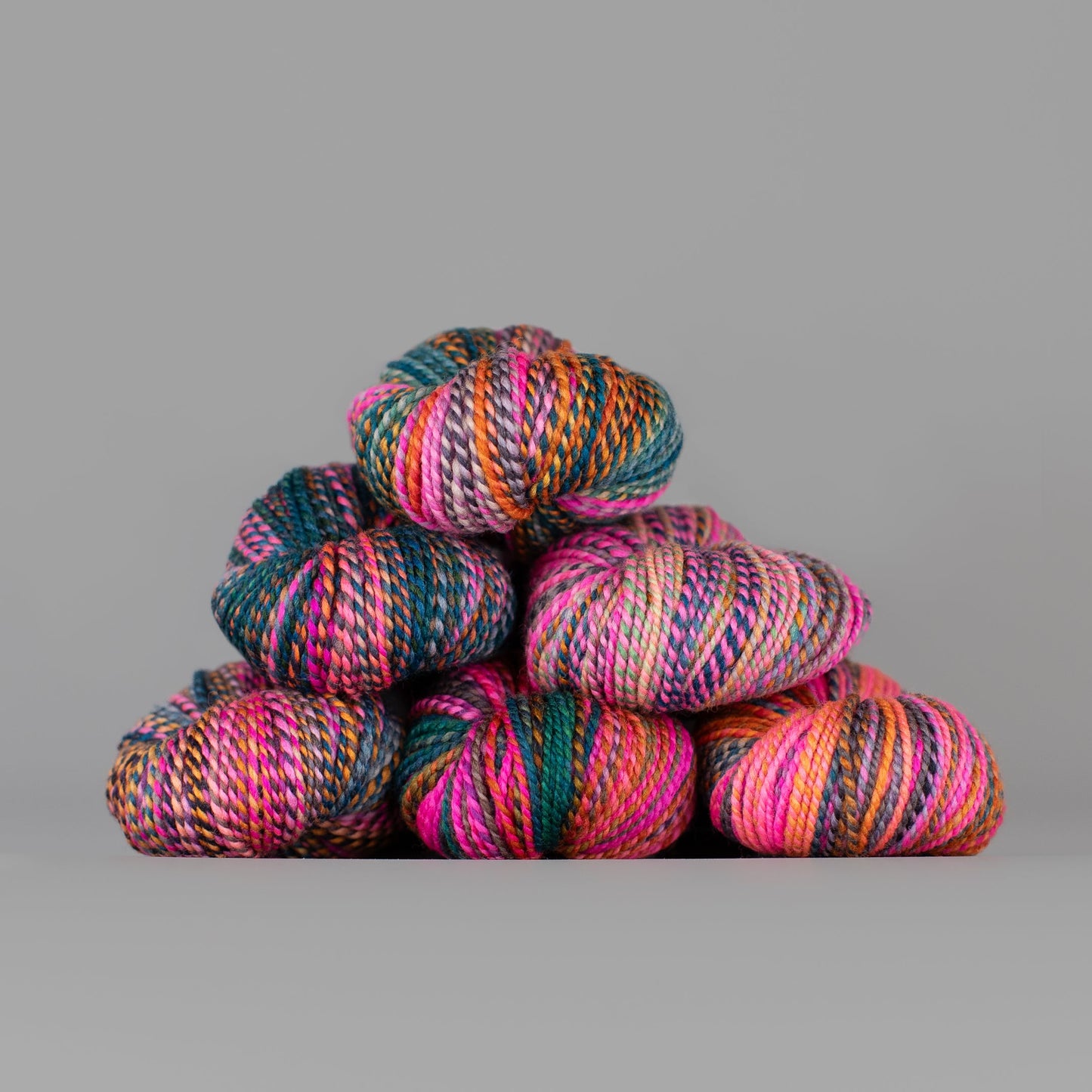 Skeins of Spincycle Dyed in the Wool sport weight yarn in a neon pink, orange, teal, and gray color gradient against a gray background.
