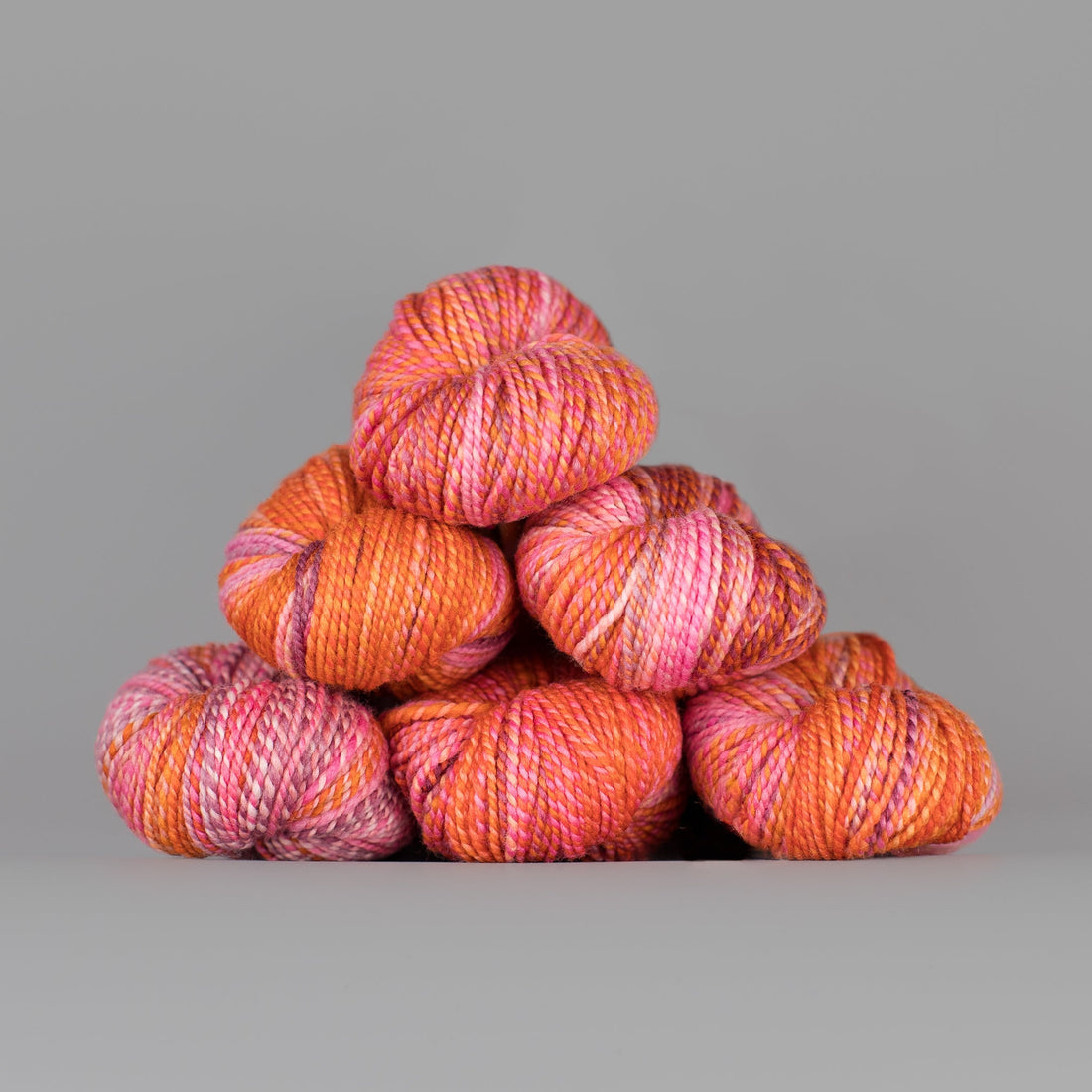 Skeins of Spincycle Dyed in the Wool sport weight yarn in a pink and orange color gradient against a gray background.
