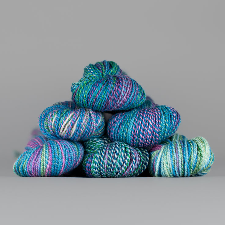Skeins of Spincycle Dyed in the Wool sport weight yarn in a blue, green, and purple color gradient against a gray background.