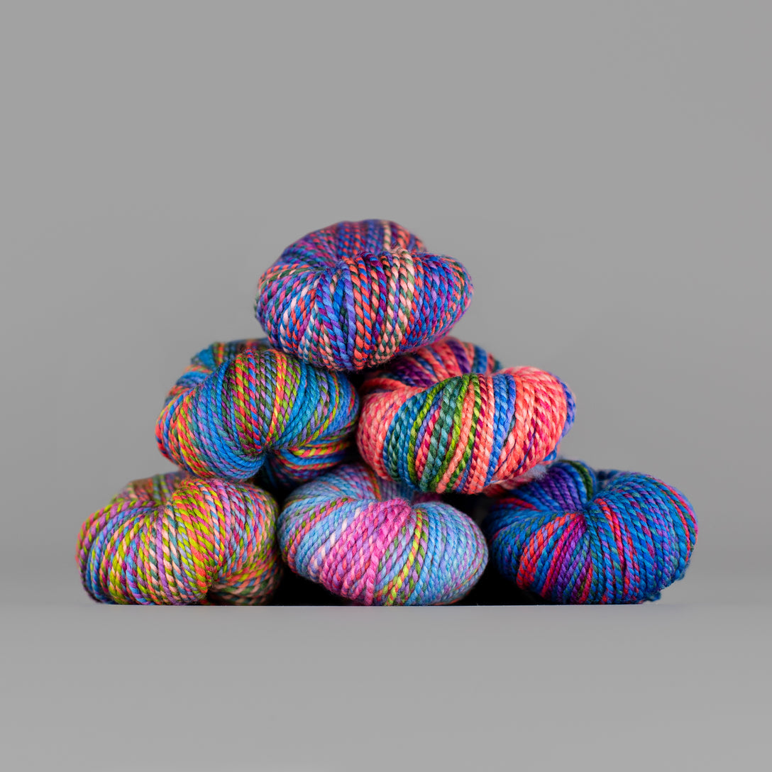 Skeins of Spincycle Dyed in the Wool sport weight yarn in a gradient of rainbow colors against a gray background.