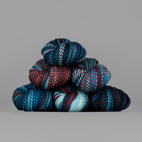 Skeins of Spincycle Dyed in the Wool sport weight yarn in a sky blue, navy, and red color gradient against a gray background.