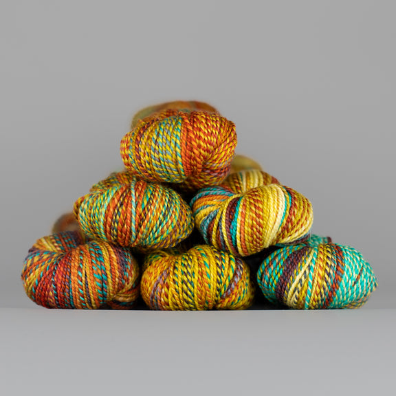 Skeins of Spincycle Dyed in the Wool sport weight yarn in a yellow, red orange, and aqua blue color gradient against a gray background.