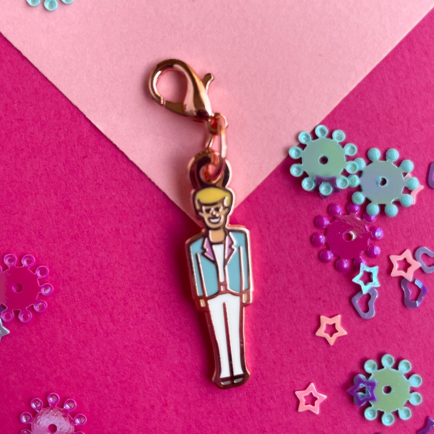 A lobster claw clasp charm shaped like a boy doll on a pink background.