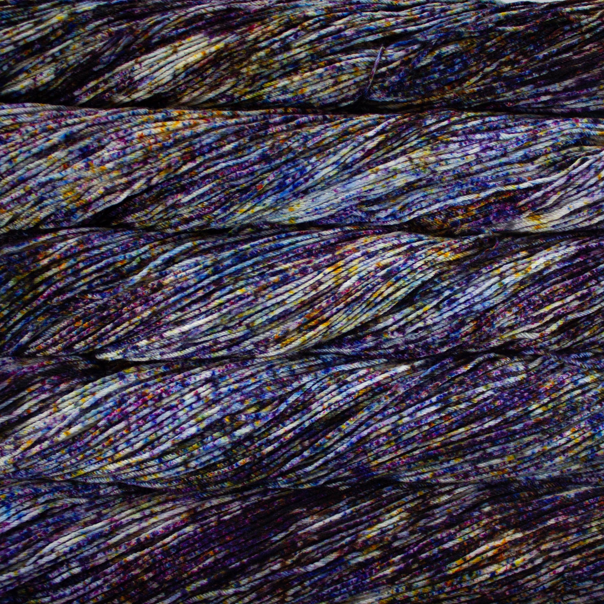 An image of skeins of Malabrigo Arroyo sport weight yarn in an off-white base with speckles of dark purple, blue, and yellow orange.
