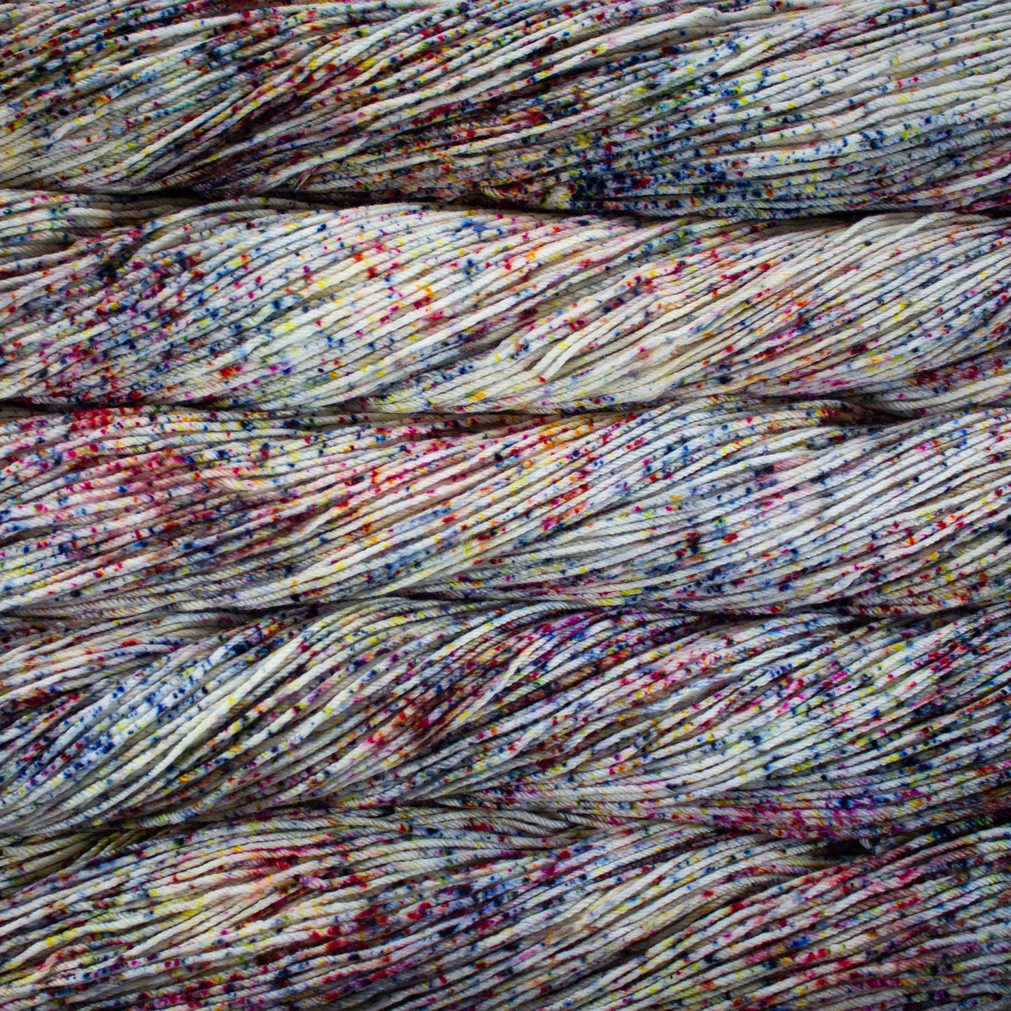 An image of skeins of Malabrigo Arroyo sport weight yarn in an off-white base with speckles of blue, red, and yellow.