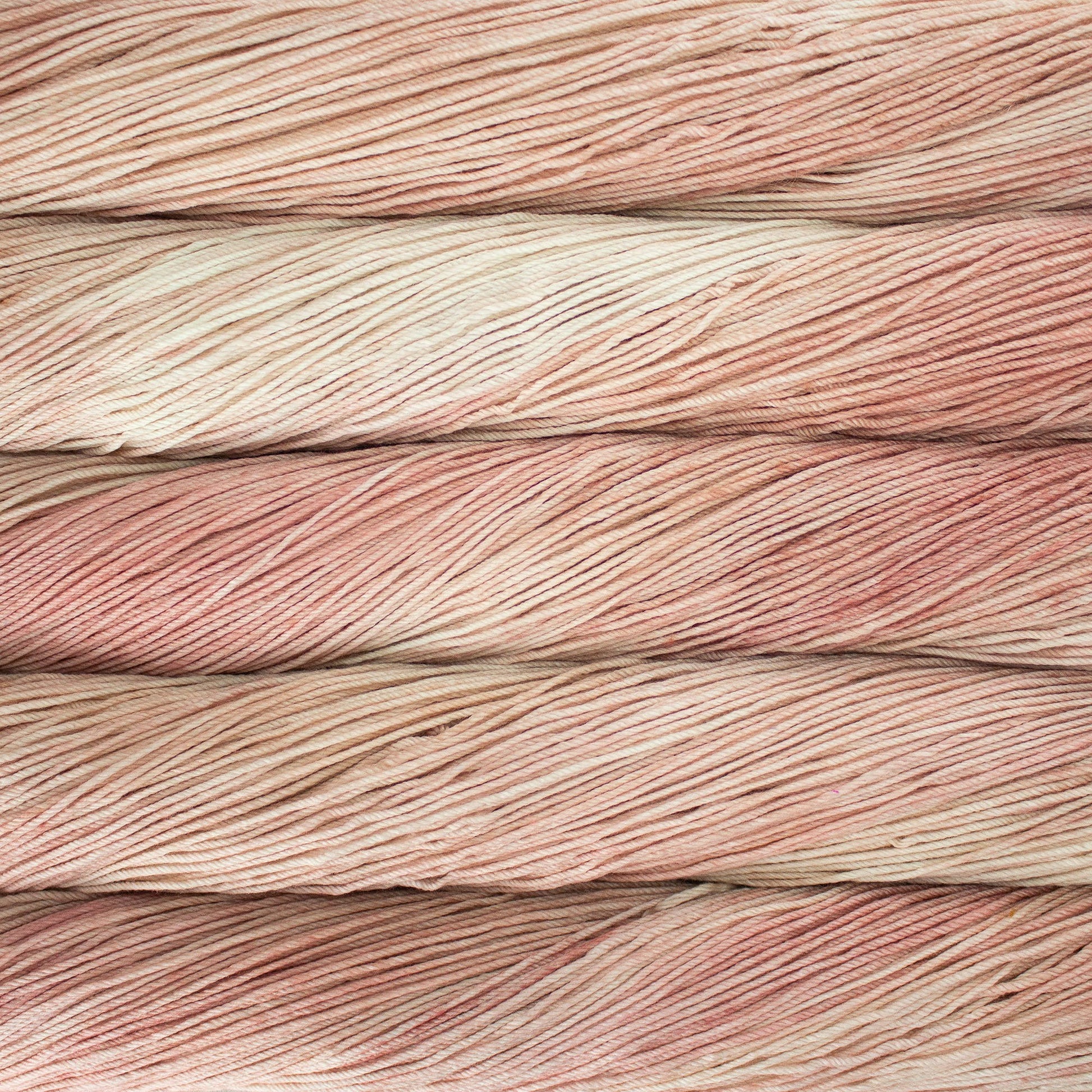 An image of skeins of Malabrigo Arroyo sport weight yarn in cream and peach pink  shades.