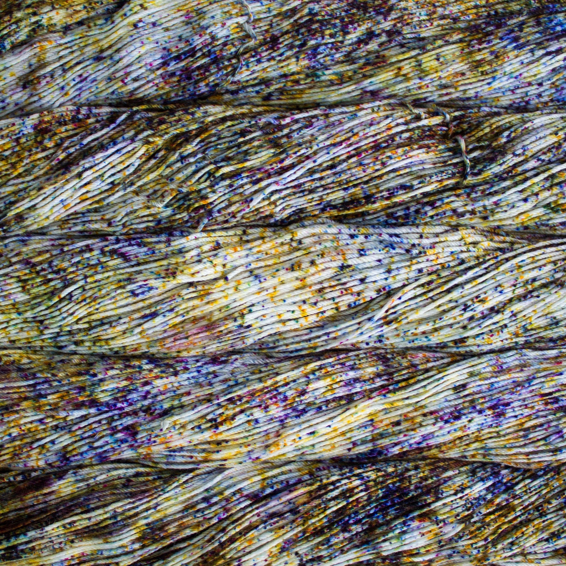 An image of skeins of Malabrigo Arroyo sport weight yarn in an off-white base with speckles of yellow, blue, and purple.