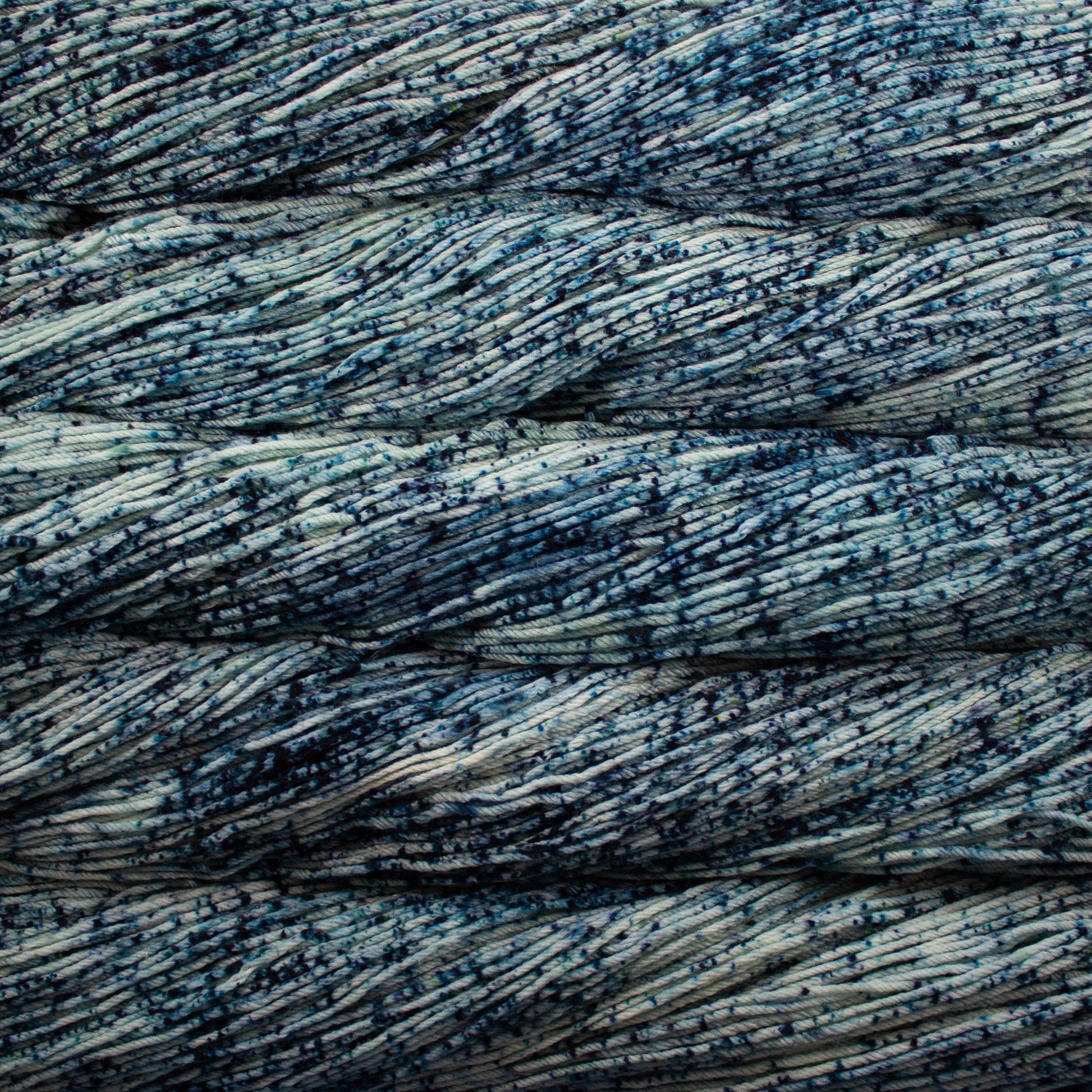 An image of skeins of Malabrigo Arroyo sport weight yarn in a light blue base with speckles of navy blue.