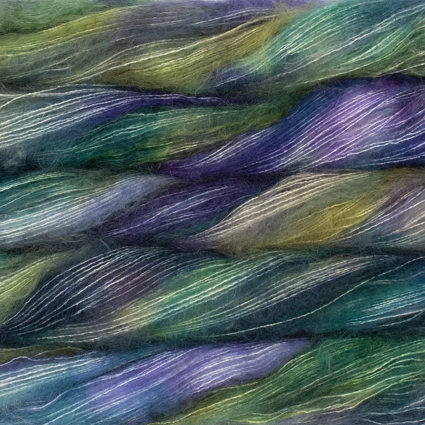 An image of multiple skeins of Malabrigo Mohair yarn in shades of green, indigo, teal, and purple.