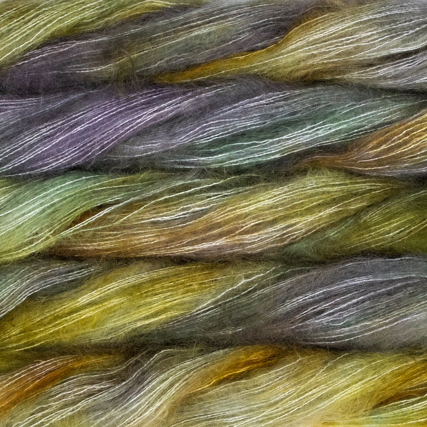 An image of multiple skeins of Malabrigo Mohair yarn in shades of yellow green and pale purple gray.