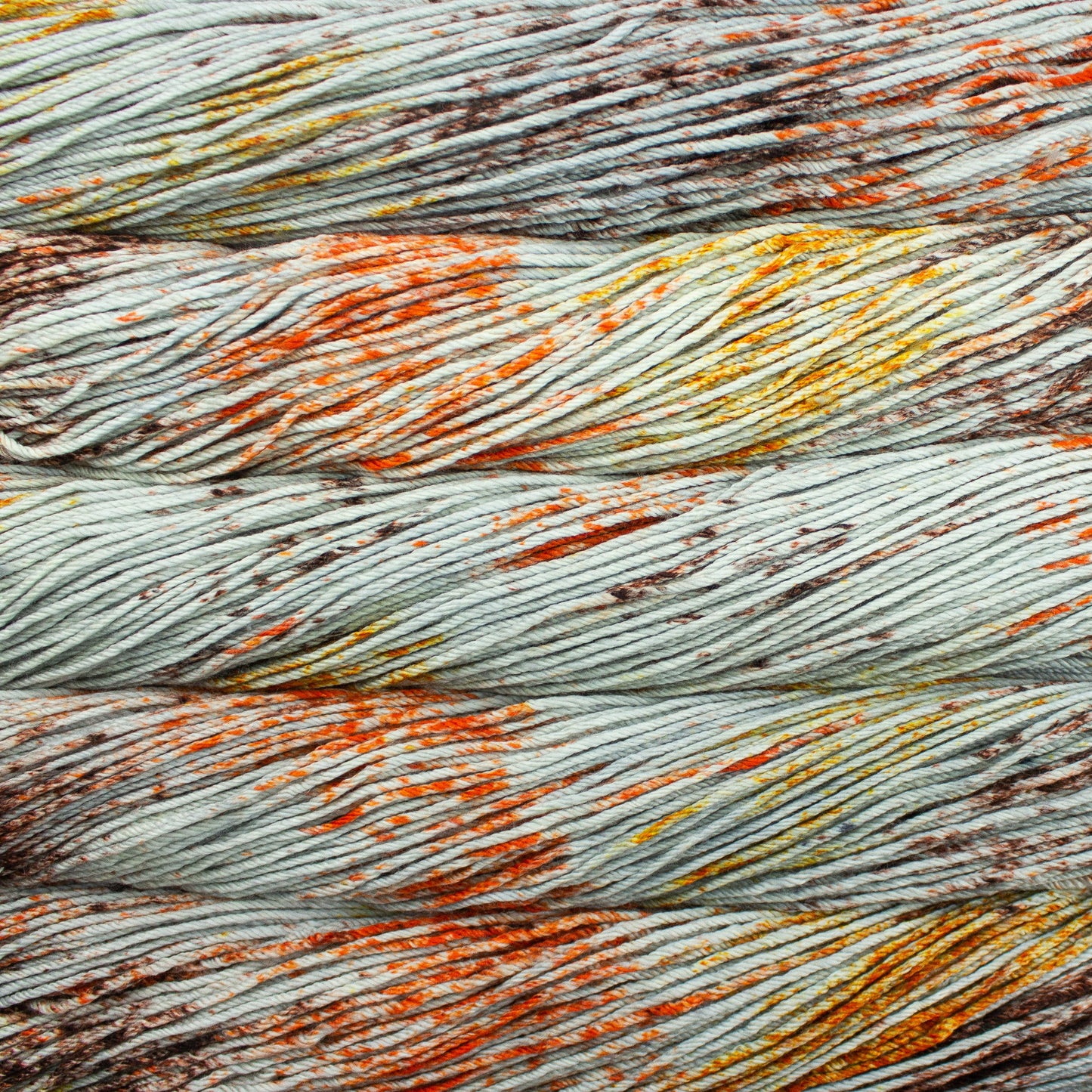 A close up of skeins of Malabrigo Rios worsted weight yarn in grey color with orange, yellow, and brown speckled colors