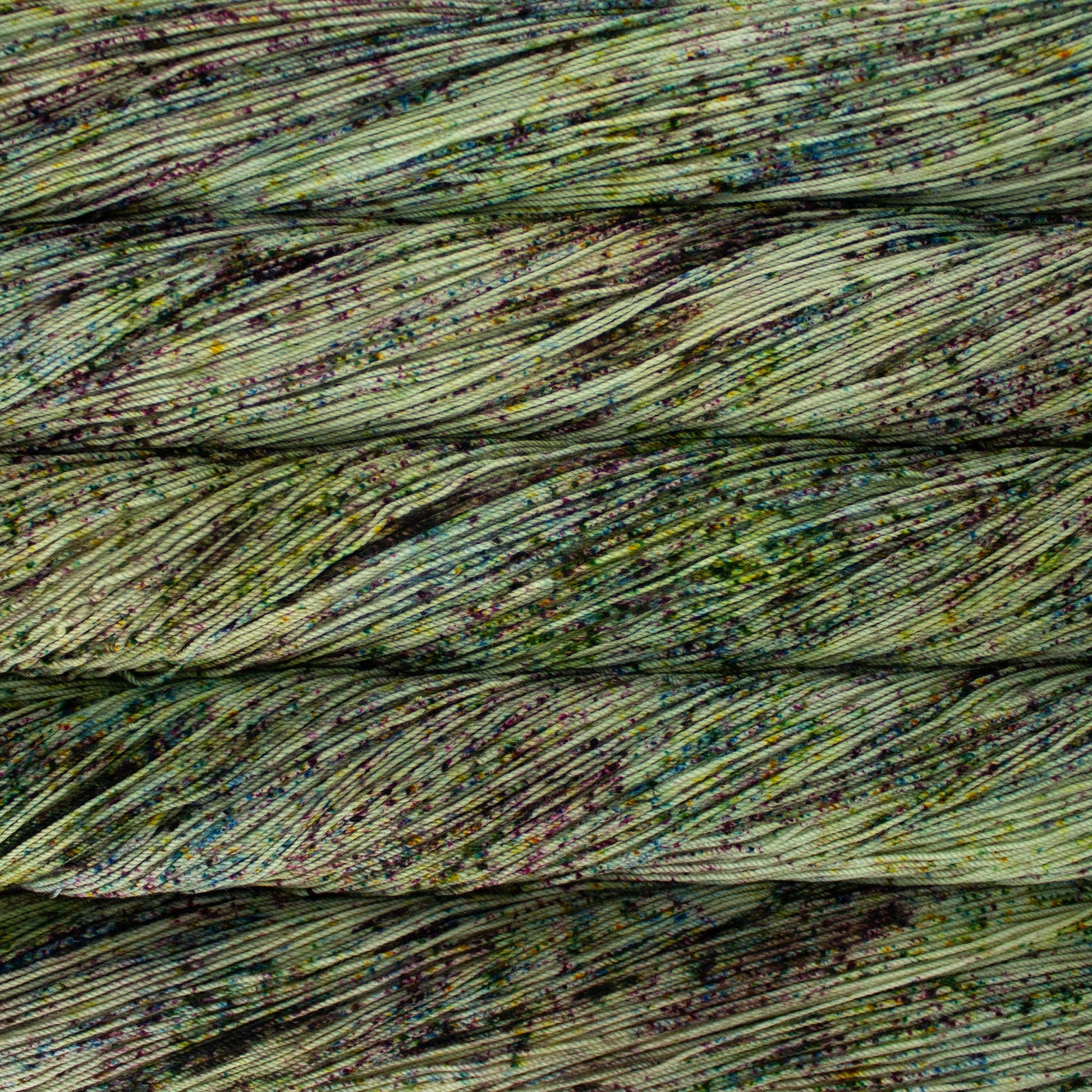 A close-up image of skeins of Malabrigo Sock yarn in a light green base with speckles of purple and teal.