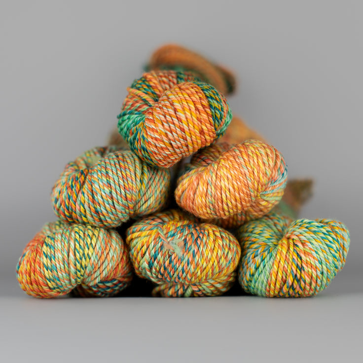 An image of skeins of Spincycle Dream State worsted weight yarn in an orange and green color gradient against a gray background.