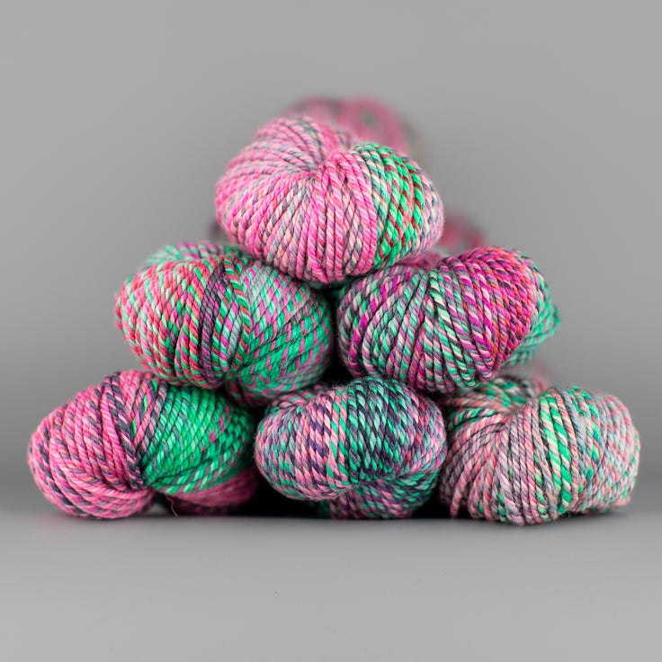 An image of skeins of Spincycle Dream State worsted weight yarn in a pink, sea green, and gray color gradient against a gray background.