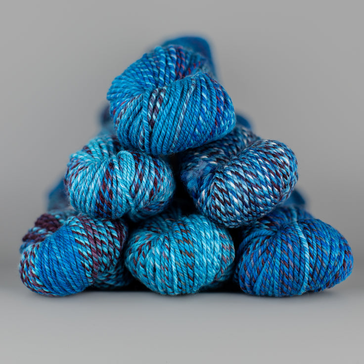 An image of skeins of Spincycle Dream State worsted weight yarn in an ocean blue and deep purple color gradient against a gray background.
