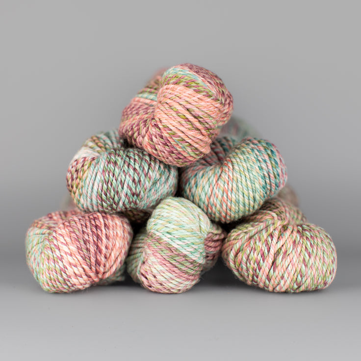 An image of skeins of Spincycle Dream State worsted weight yarn in a peach and mint green color gradient against a gray background.